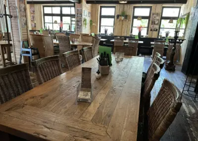 Ein großer Holztisch mit Rattanstühlen in einem Restaurant mit mehreren Fenstern.