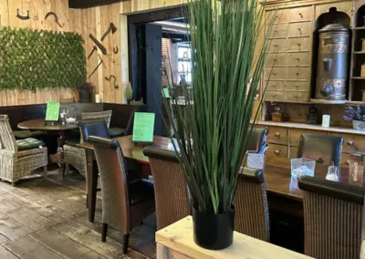 Künstliche Pflanze in einem schwarzen Topf steht auf einem Tisch in einem Restaurant mit Holzmöbeln.