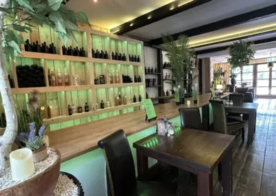 Holzregal mit Flaschen und Pflanzen in einem Restaurant, das eine gemütliche Atmosphäre ausstrahlt.