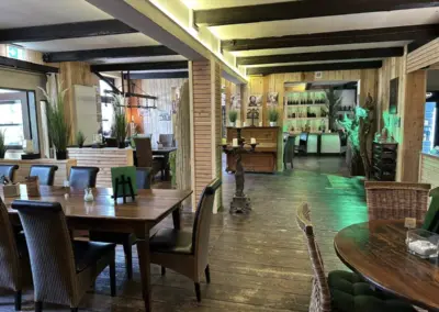 Innenansicht eines Restaurants mit Holztischen und Stühlen sowie dekorativen Elementen.